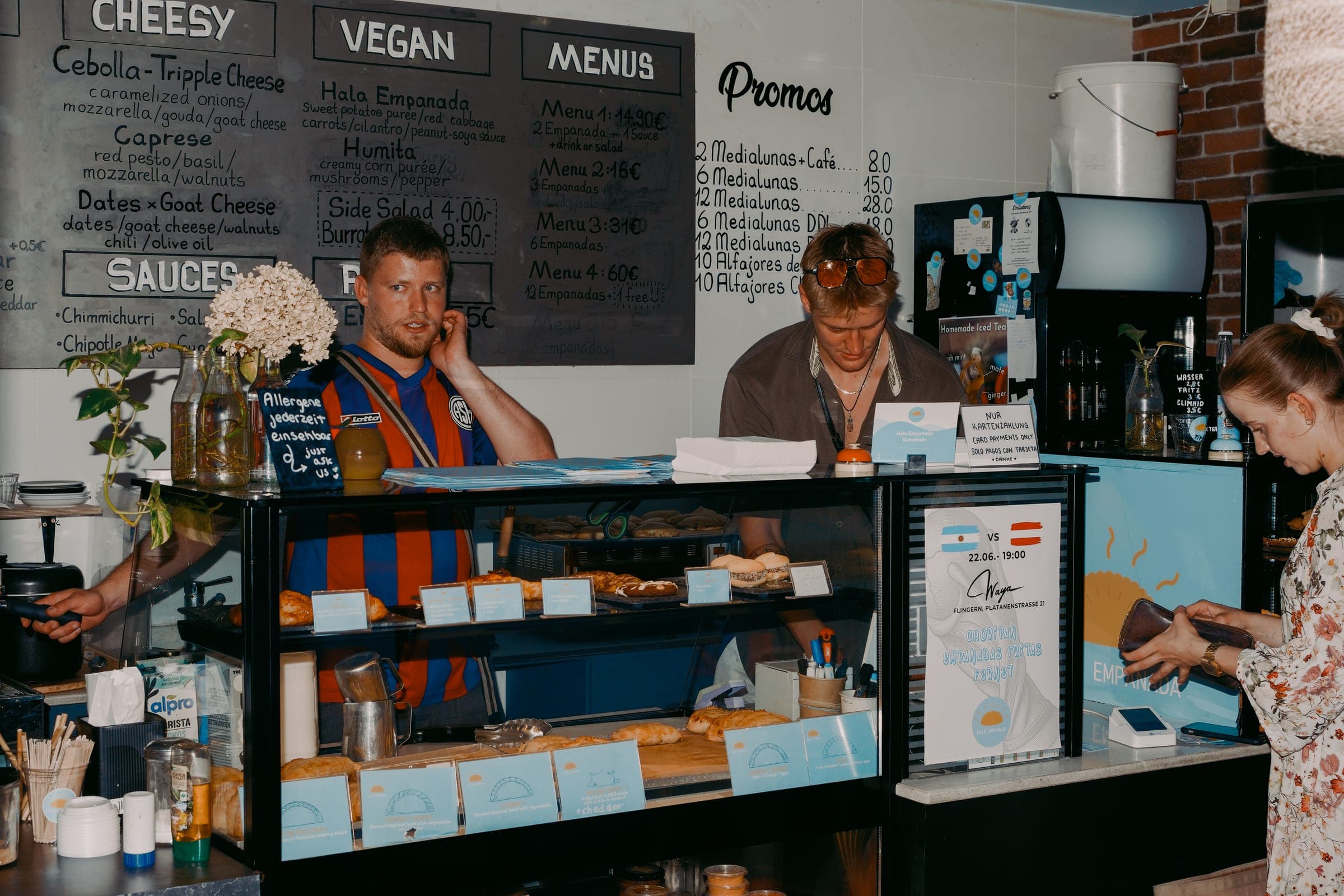 Das Hala Team hinter der Theke mit Empanada-Vitrine und Menütafel